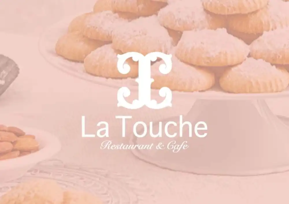 A beautifully arranged plate of cookies on a white stand, featuring the La Touche logo in elegant script, emphasizing the restaurant and cafe's charm.