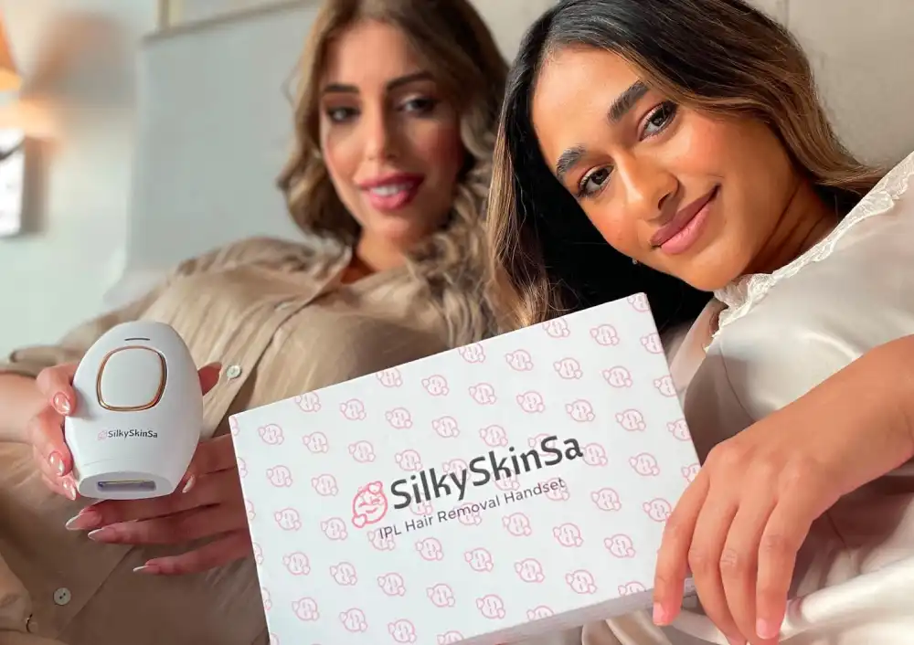 Two women happily posing with a Silky Skin IPL hair removal handset and its packaging, showcasing the product's sleek design and branding.