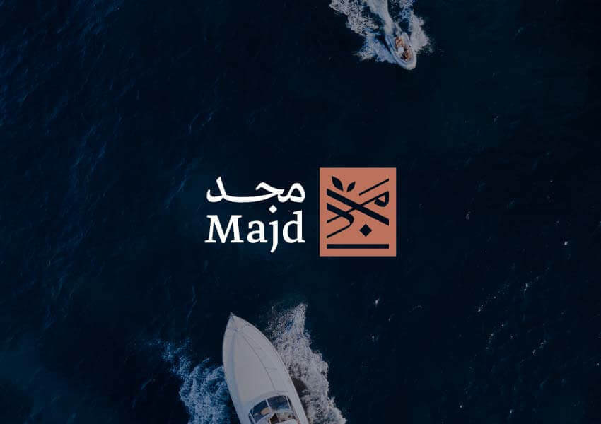 An aerial view of a boat gliding over deep blue waters, accompanied by the Majd logo featuring Arabic text and a distinctive emblem.