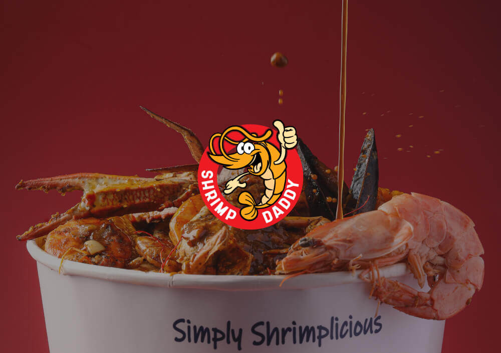 Bucket of seafood from Shrimp Daddy KSA with their logo on top and a sauce being poured over shrimp, crab, and mussels