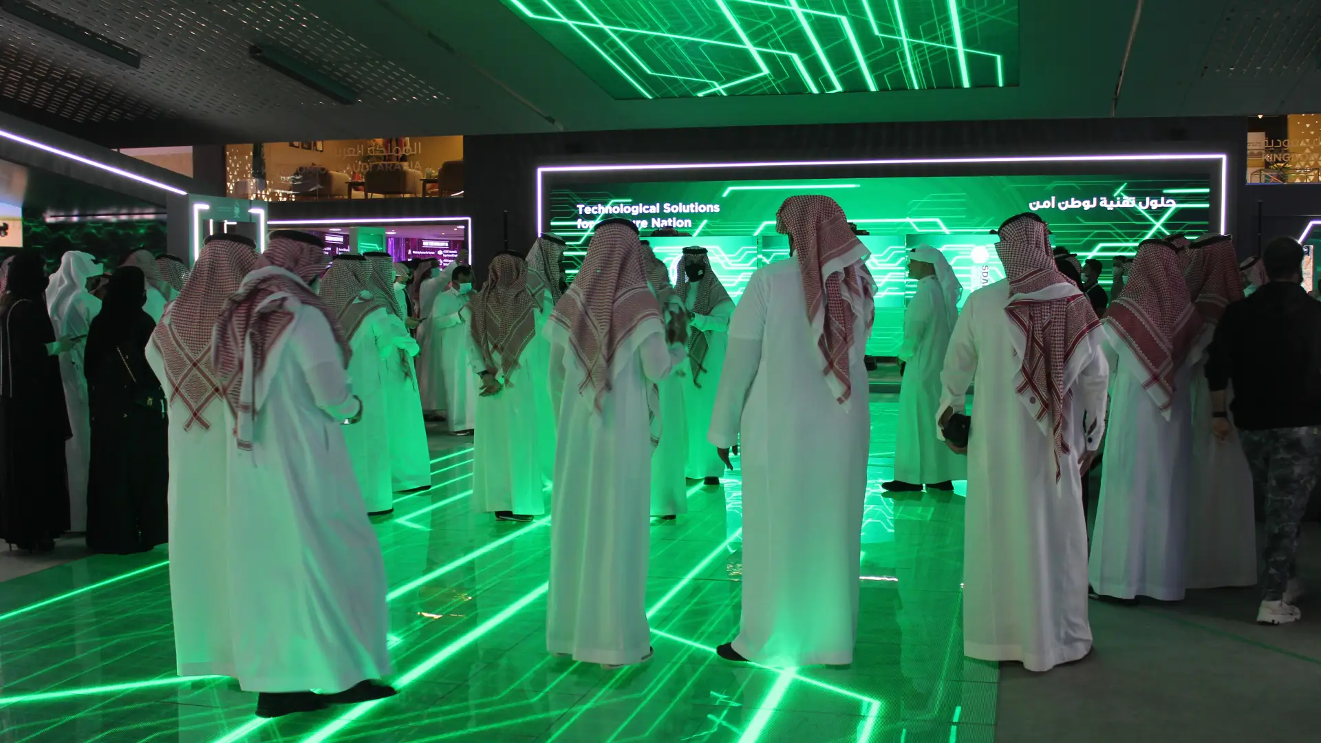 A large group of men and women in traditional attire gathering at a technology-themed career fair in Saudi Arabia, illuminated by green lights. career fair career fair Saudi Arabia career fair Riyadh a Step Ahead career fair employment fair